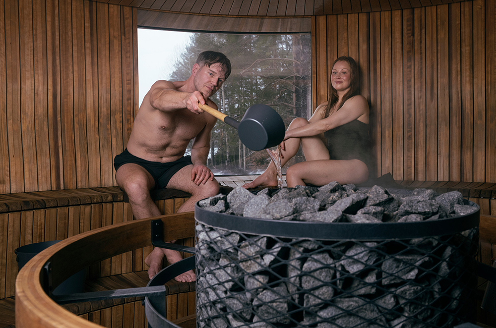 Man throws hot water on rocks in a wood sauna, showing the significance of sauna in Finnish culture and design